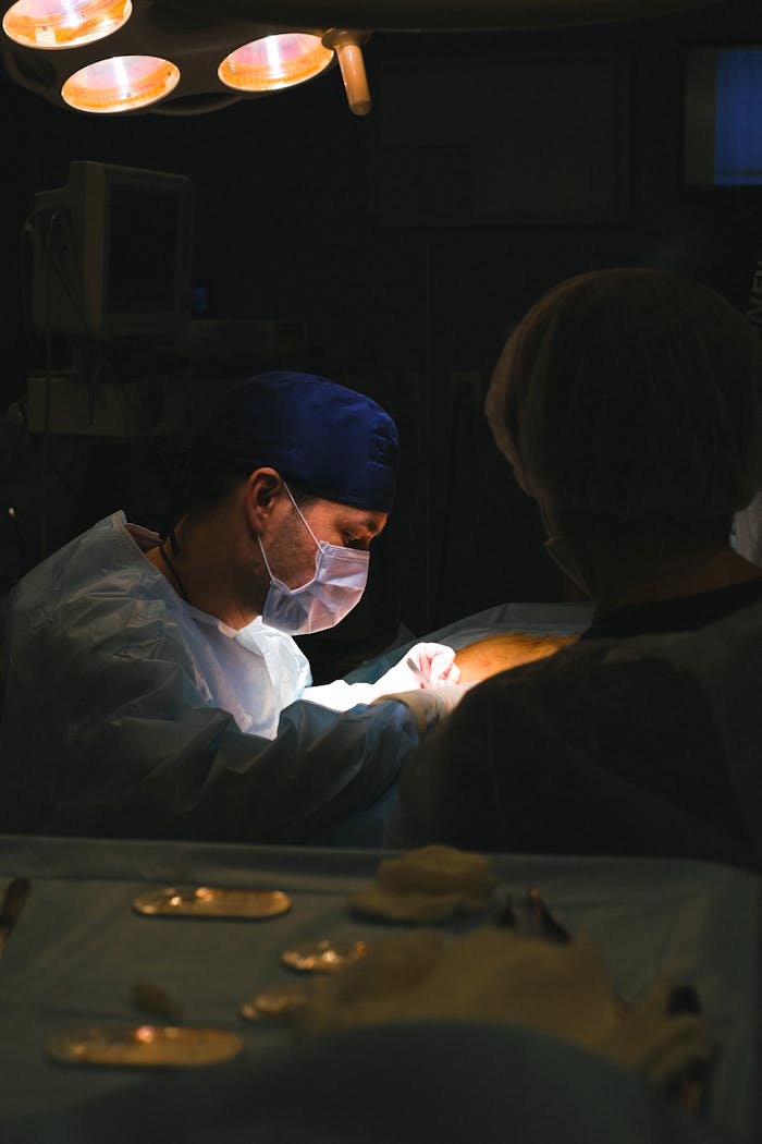 A surgeon in an operating room focused on a procedure under surgical lights.